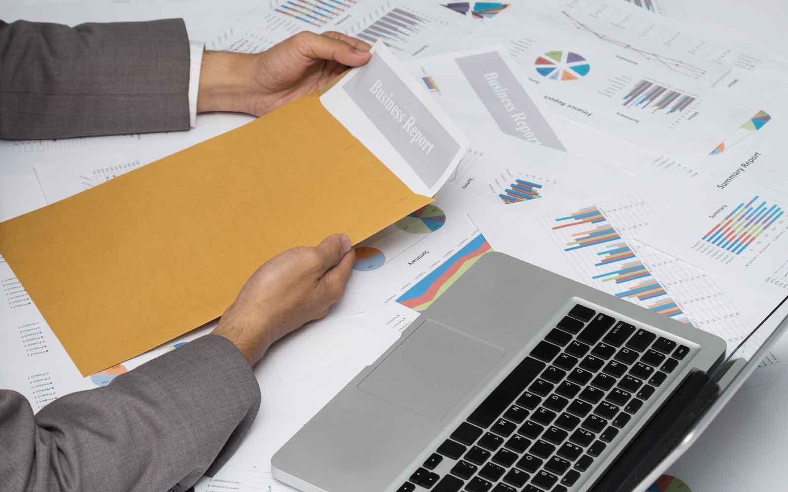 Person reviewing business reports and charts beside a laptop
