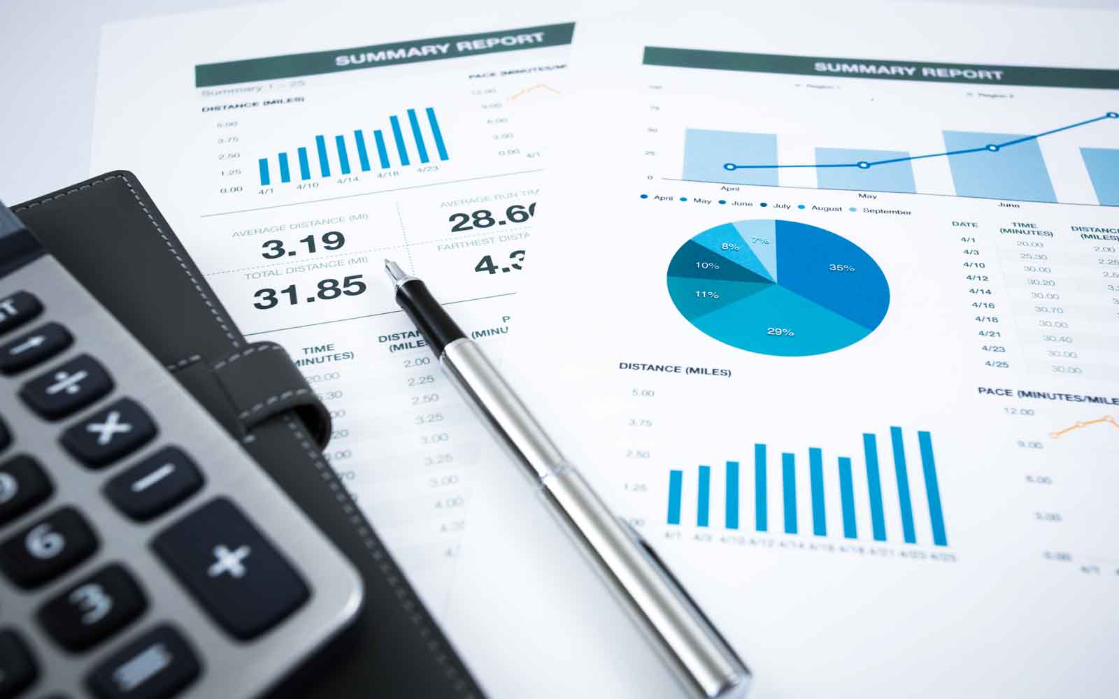 Calculator and pen resting on business reports with bar, line and pie charts